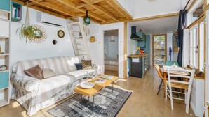 A cozy living room with a sofa, coffee table, and a dining area with chairs. There is a staircase leading to an upper level, and a kitchen area is visible in the background. - Les Cabanes de Mamette - sur les hauteurs de Beaune (Beaune)