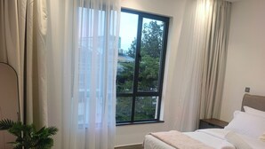 Ein Schlafzimmer mit einem großen Bett, einem Fenster mit Vorhängen, einer Topfpflanze und Holzdielen.