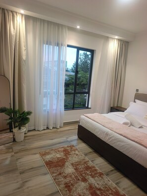 Un dormitorio con una cama grande, una ventana con cortinas, una planta en maceta y suelo de madera.