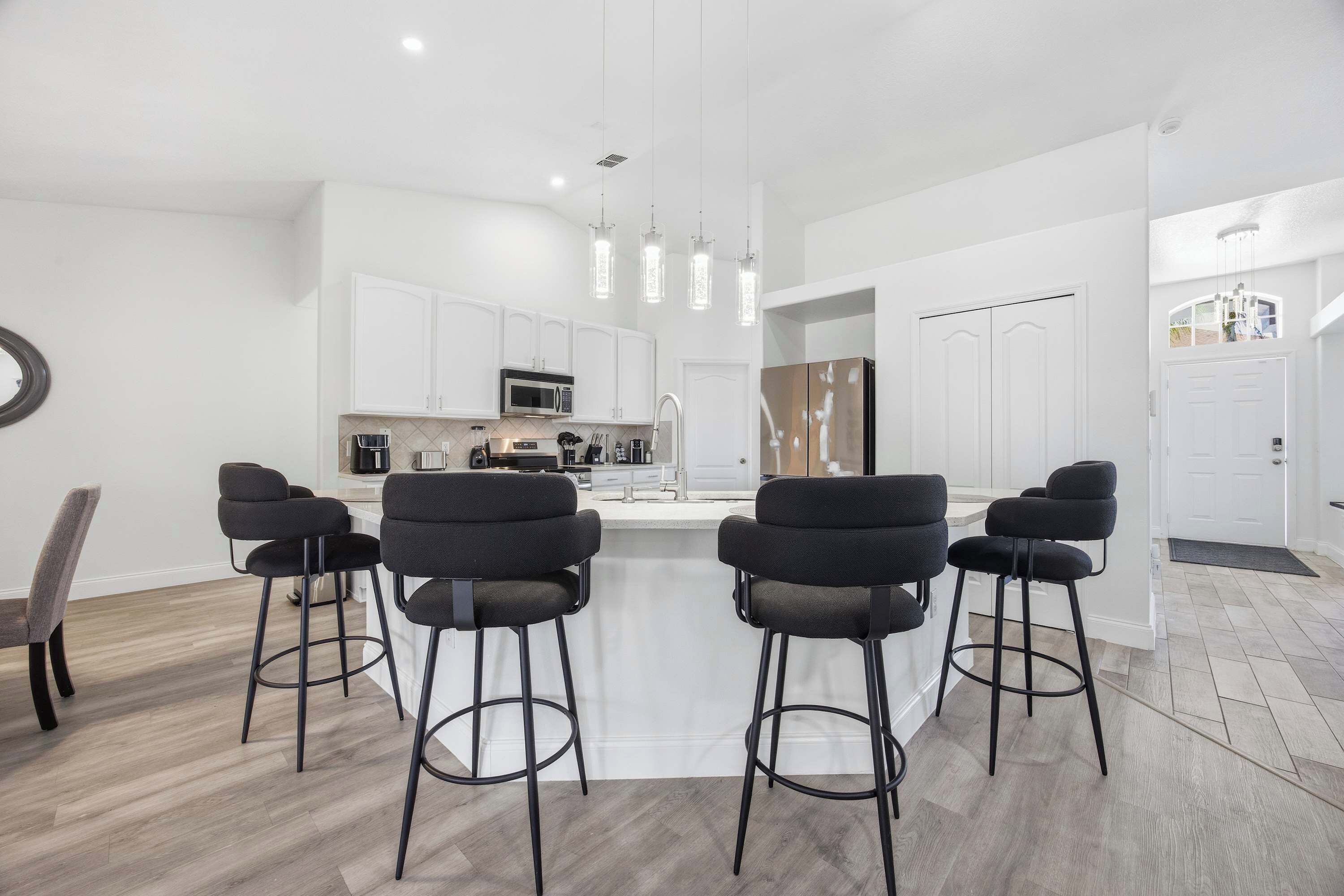 Una cocina moderna con armarios blancos, una isla central con taburetes y lámparas colgantes.