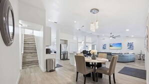 Una cocina moderna con una isla central, un comedor con una mesa redonda y sillas, y una escalera que sube a otro nivel.