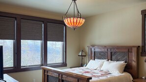 A bedroom with a wooden bed, a hanging light fixture, a window with blinds, and a round rug. - Lodge with Incomparable Views & Direct Ski Access (Whitefish)