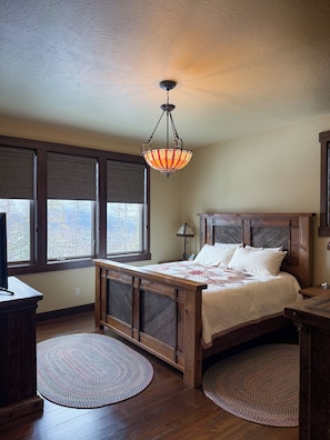 A bedroom with a wooden bed, a hanging light fixture, a window with blinds, and a round rug.