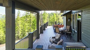 A wooden deck with outdoor furniture, a railing, and a view of a forest. - Lodge with Incomparable Views & Direct Ski Access (Whitefish)