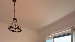 Una habitación con piso de madera, un televisor sobre un mueble bajo, un banco, una estantería y una ventana con vistas a edificios.