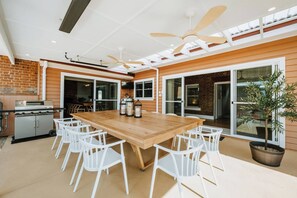 A spacious dining area with a large wooden table, white chairs, and a ceiling fan.