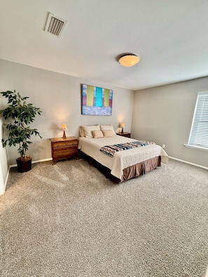 A bedroom with a bed, two nightstands, a potted plant, a ceiling vent, a wall-mounted painting, and a window with blinds. - Charming 3BR home with big yard, across park and lake in Grand Prairie (Grand Prairie)