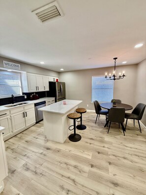 A modern kitchen with white cabinets, a central island, and a dining area with a chandelier. - Charming 3BR home with big yard, across park and lake in Grand Prairie (Grand Prairie)