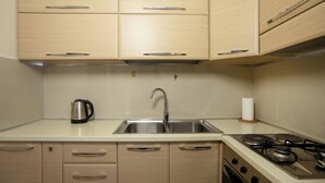 A kitchen with a stainless steel sink, a kettle, a stove, and wooden cabinets. - Sea Point Apartments (Durrës)