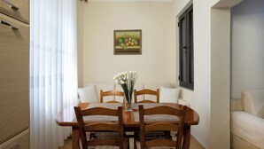 A dining area with a wooden table, four chairs, a vase with flowers, a painting on the wall, and a window with curtains. - Sea Point Apartments (Durrës)
