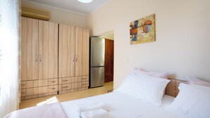 A bedroom with a bed, a wardrobe, a refrigerator, and a painting on the wall. - Sea Point Apartments (Durrës)