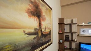 A living room with a large landscape painting, wooden shelves, a flat-screen TV, and a Wi-Fi sign. - Sea Point Apartments (Durrës)