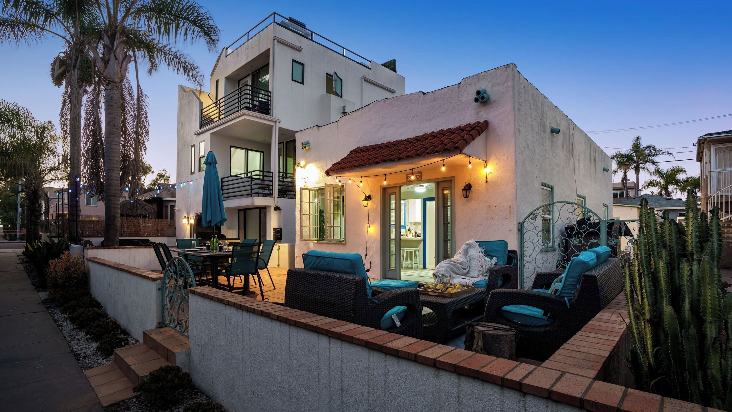 A modern two-story house with a patio area featuring outdoor furniture and string lights.