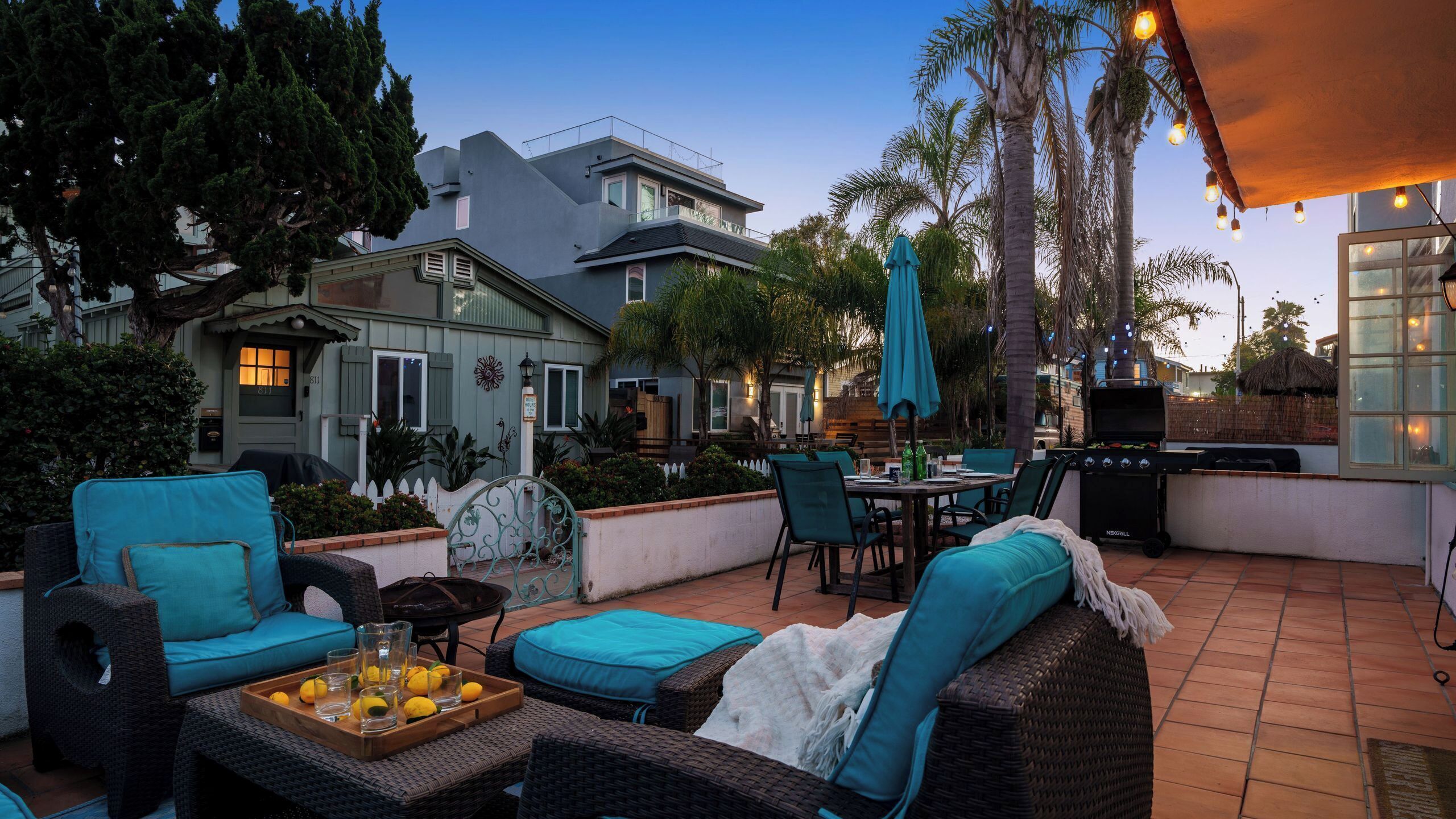 An outdoor patio with wicker furniture, a grill, and a view of a house in the background.