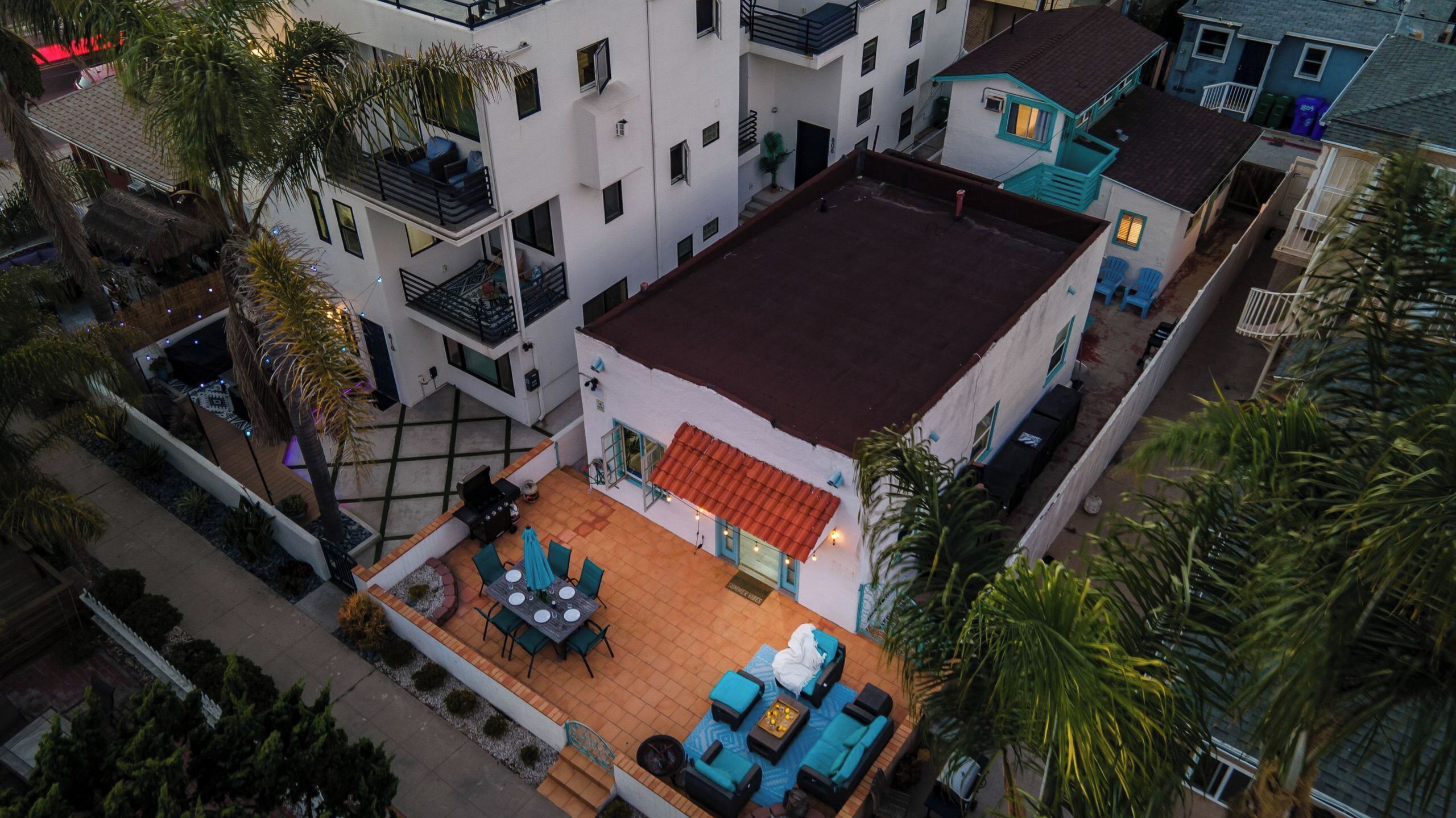 Ein Luftbild eines Wohnhauses mit Dachterrasse, mehreren Balkonen und umgebender Bepflanzung.
