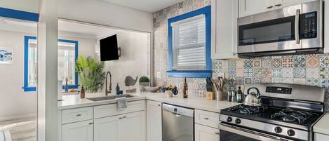 A modern kitchen with white cabinets, a stainless steel dishwasher, a gas stove, and a microwave.