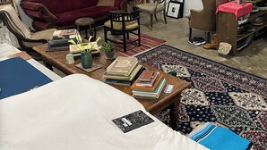 A cozy living room with a red sofa, a wooden coffee table with books, a bookshelf, and a dining area with a pink tablecloth. - Artist’s Studio Steps from Sunset Plaza. Prime West Hollywood Location (West Hollywood)