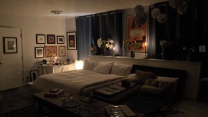 A dimly lit bedroom with a large bed, bedside tables, a dresser, and a window with curtains. - Artist’s Studio Steps from Sunset Plaza. Prime West Hollywood Location (West Hollywood)