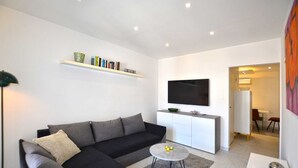 Una sala de estar moderna con un sofá negro, una mesita de centro redonda, un televisor de pantalla plana y una estantería.
