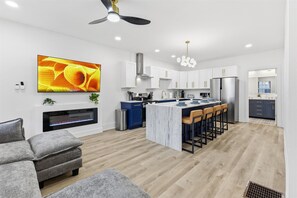 A modern kitchen with white cabinets, a central island with bar stools, a built-in oven, and a ceiling fan. - Newly Renovated 4 BR near downtown Indy w Garage! (Indianapolis)