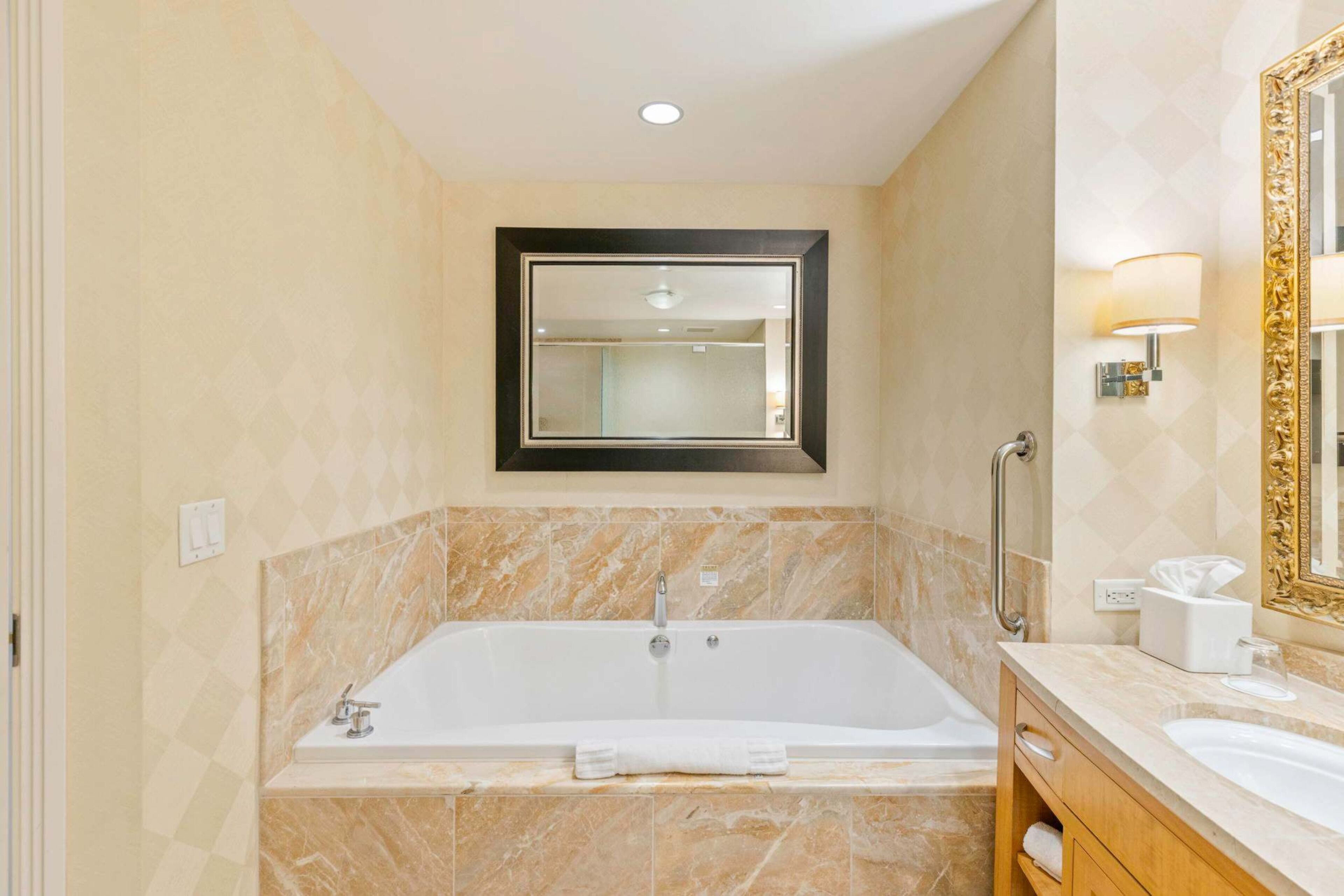 Une salle de bain moderne avec une grande baignoire, un meuble-lavabo avec un miroir et un porte-serviettes.