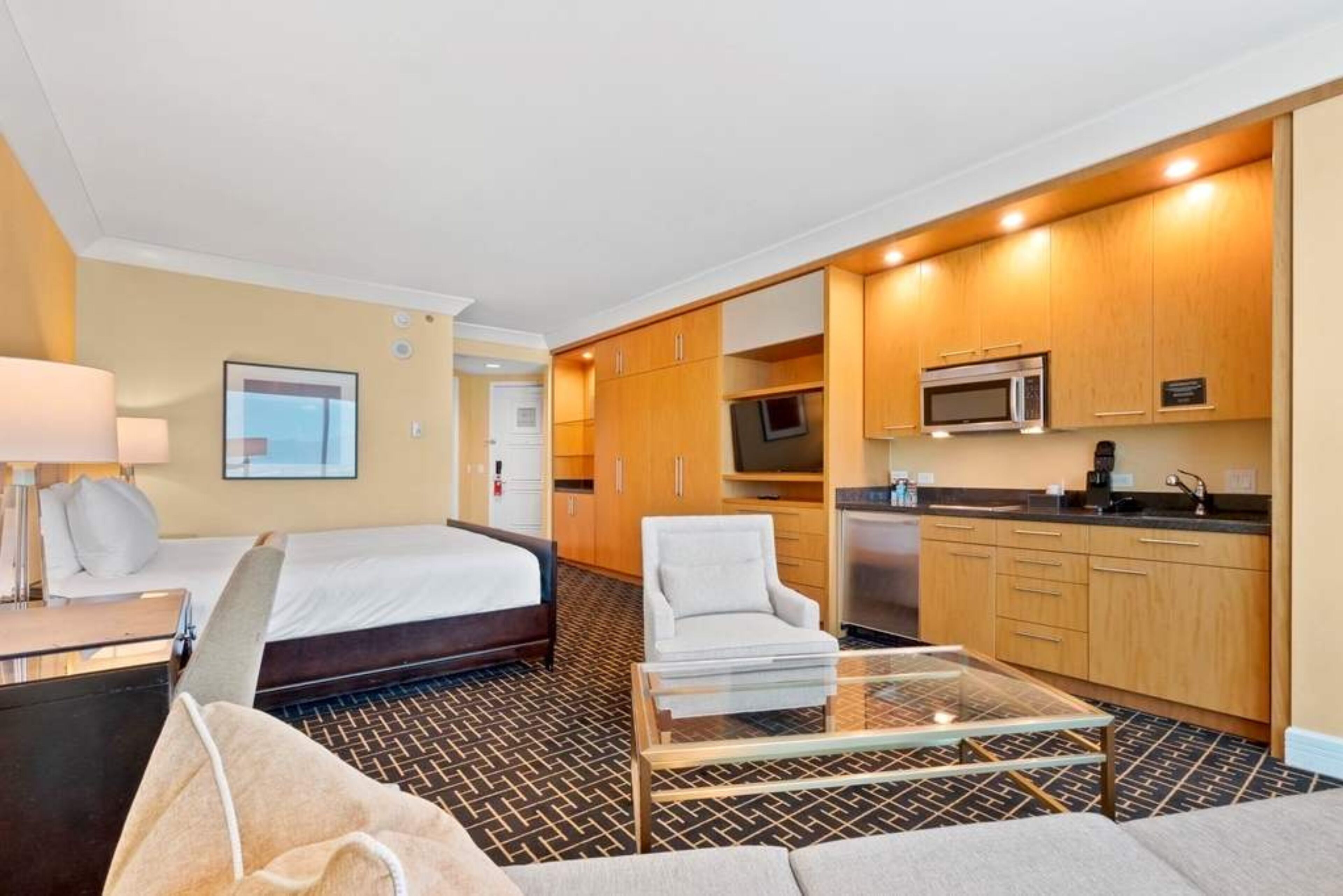 Une chambre d’hôtel comprenant un lit, un canapé, une table basse en verre, une télévision, un four à micro-ondes et une kitchenette.