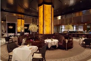 A hotel lobby with round tables, sofas, and a bar area. - Trump Studiio (Las Vegas)