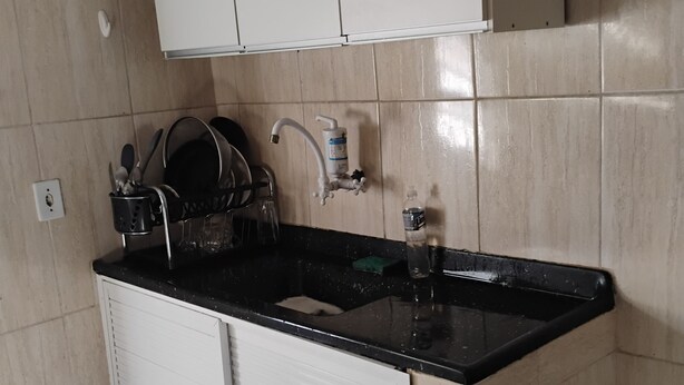 A kitchen with a black countertop, white cabinets, a sink, and a trash can.