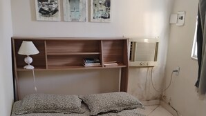 A bedroom with a bed, a nightstand, a lamp, a shelf with books, and wall art.