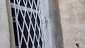 A white metal gate with a diamond pattern, attached to a concrete wall with visible wear and a small pipe.