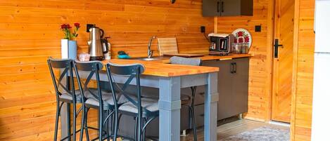 Interior em madeira com cozinha, incluindo uma mesa com cadeiras, uma cafeteira e um armário.