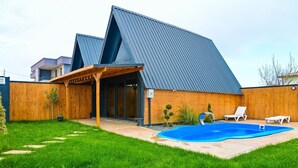 Ein modernes Haus mit Swimmingpool, Holzterrasse und überdachter Terrasse.
