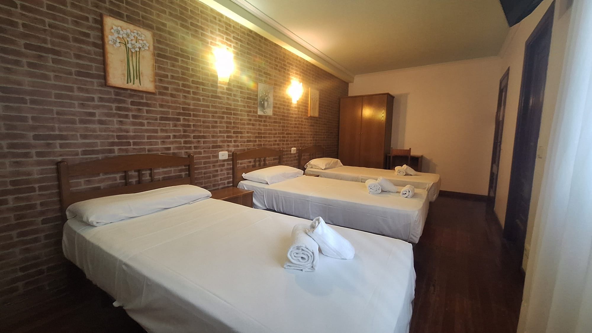 Ein Hotelzimmer mit drei Betten, einer Ziegelwand und Wandleuchten.