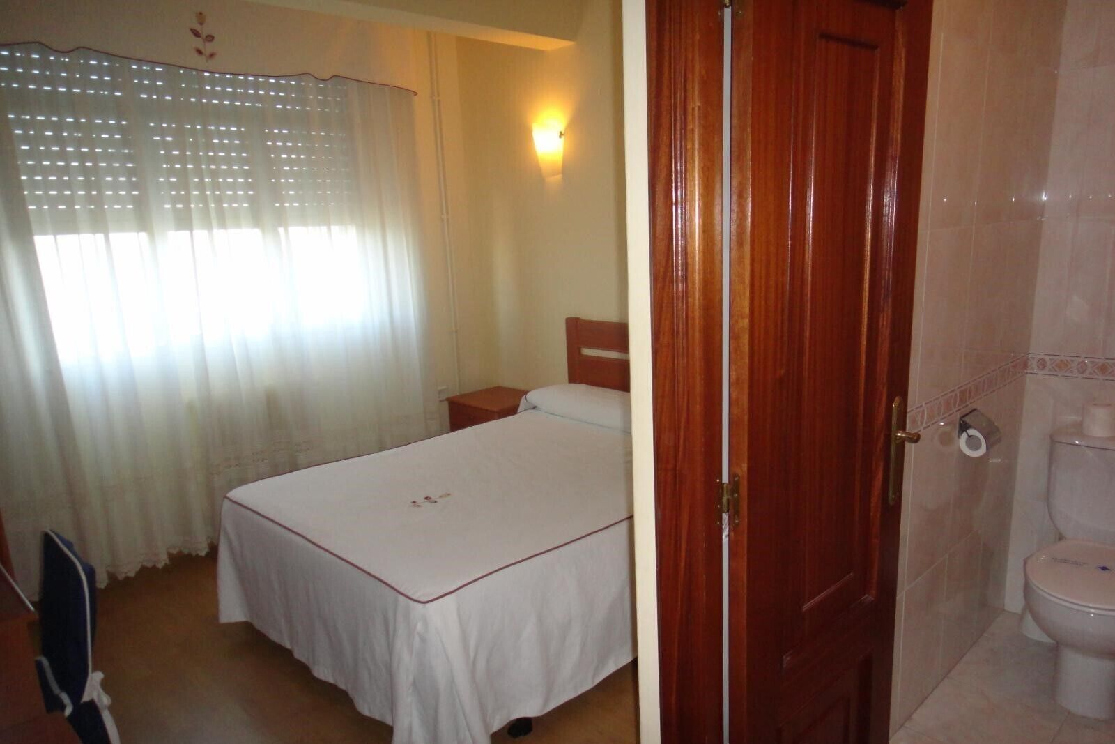 Un dormitorio con cama, mesita de noche, puerta de madera y baño con inodoro.