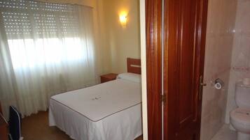 Un dormitorio con cama, mesita de noche, puerta de madera y baño con inodoro.