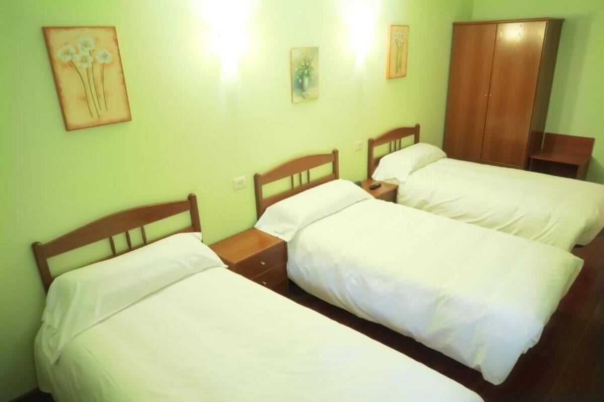 A room with three single beds, wooden headboards, a wardrobe, and artwork on the walls.