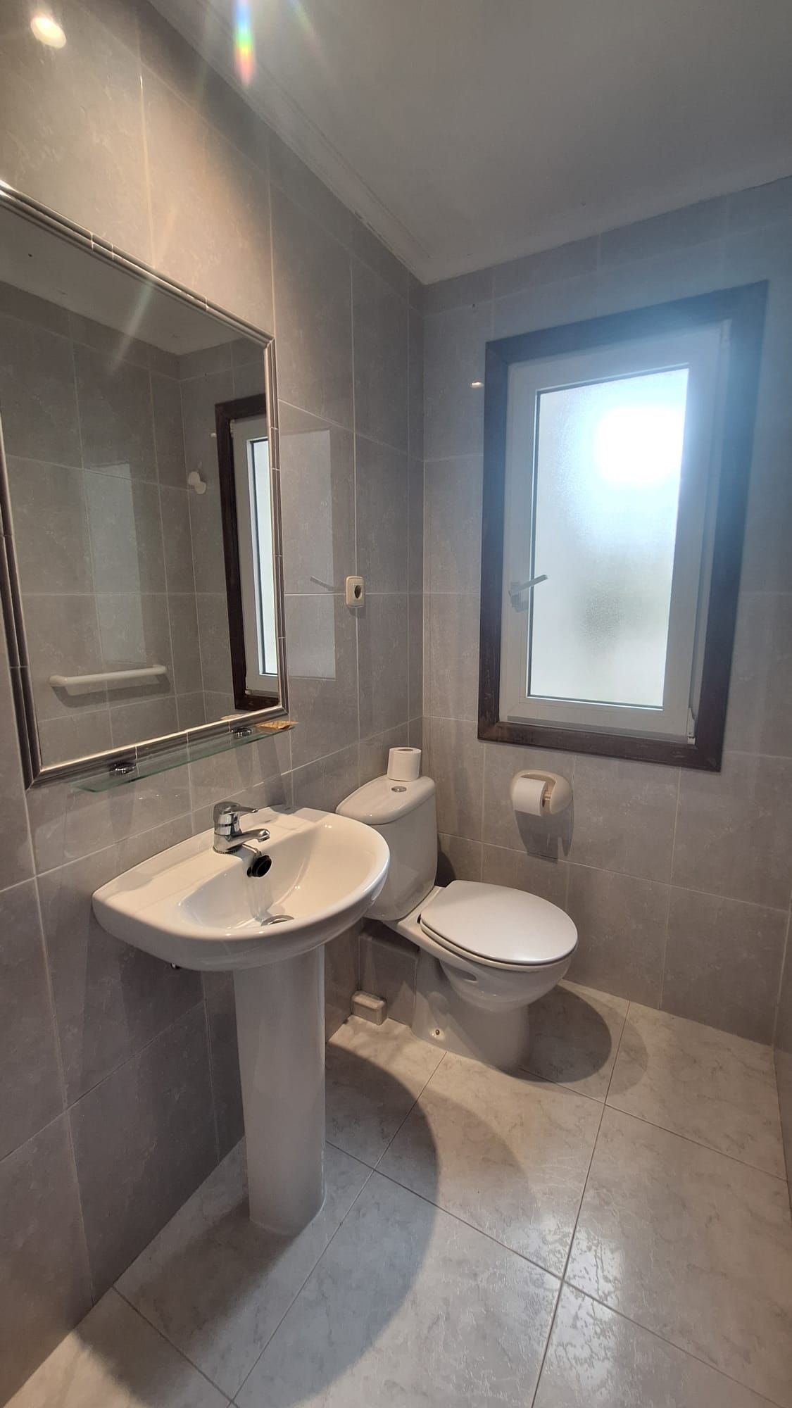 A bathroom with a pedestal sink, toilet, and a window with frosted glass.