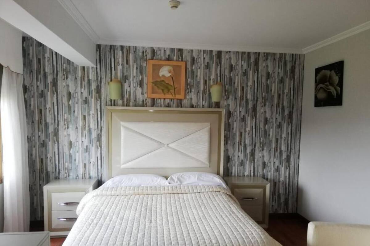 A bedroom with a large bed, two bedside tables, a headboard, and a wall with vertical patterned wallpaper.