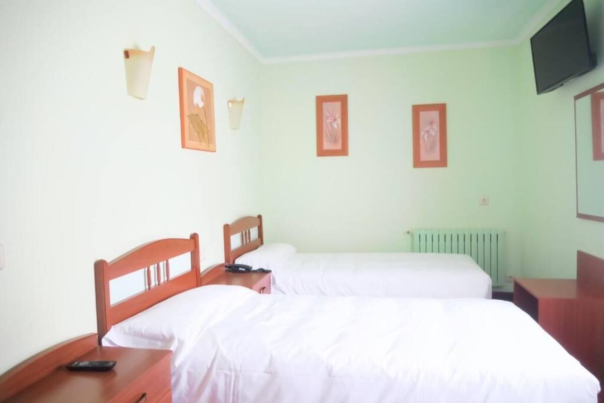 A room with two beds, a wooden nightstand, a wall-mounted TV, and framed pictures on the wall.