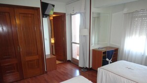 A hotel room with wooden flooring, a bed, a desk, a chair, a TV, and a window with curtains. - My Rooms Hotel Camiño do Mar (Rois)