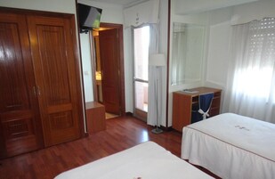 Habitación de hotel con suelo de madera, una cama, un escritorio, una silla, un televisor y una ventana con cortinas.