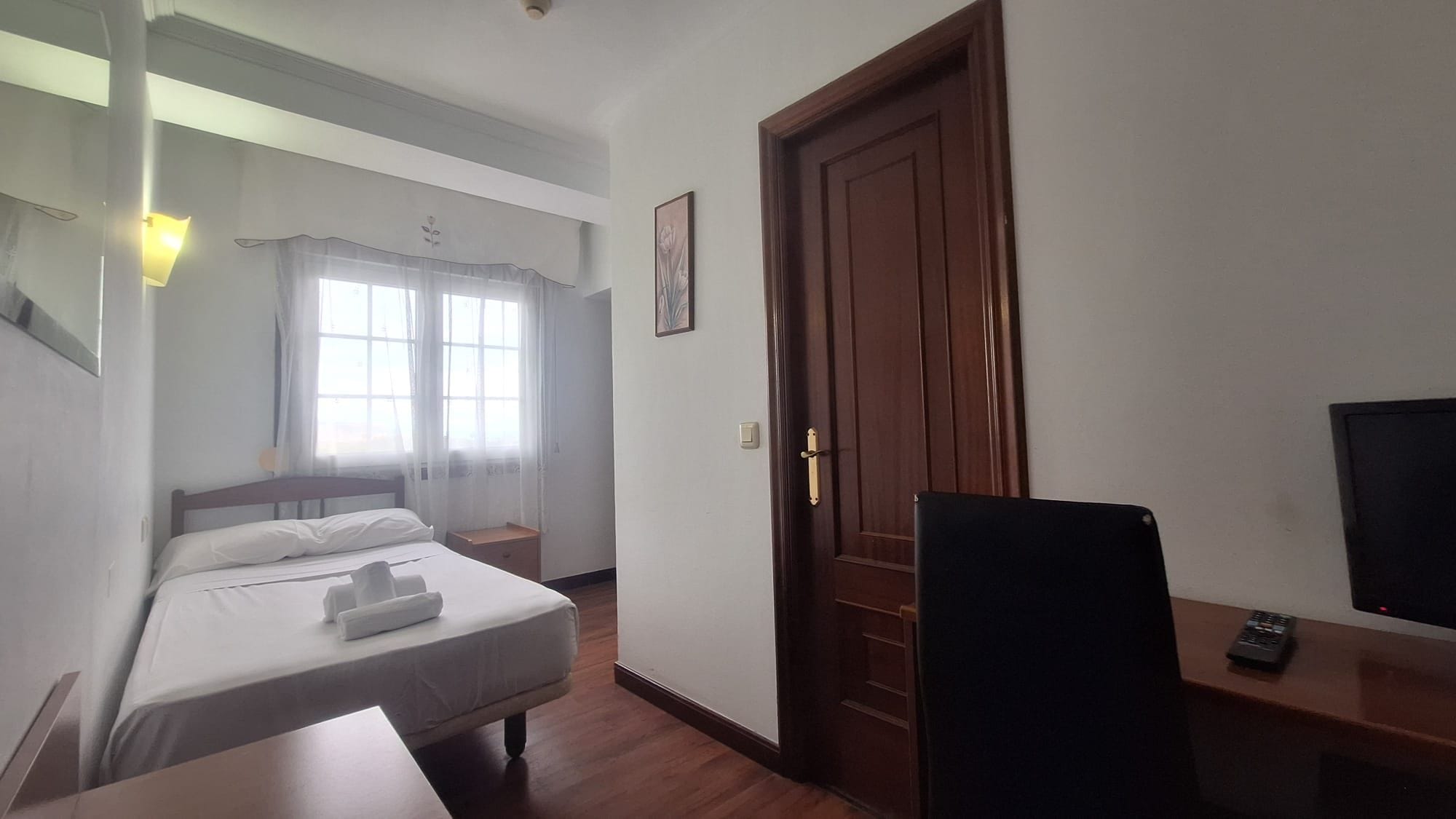Una habitación de hotel con cama, escritorio, televisor y puerta.