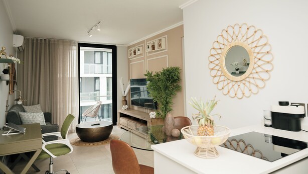 Een moderne woonkamer met een bank, stoelen, een salontafel, een televisie, een grote spiegel en een eethoek met een tafel en stoelen.