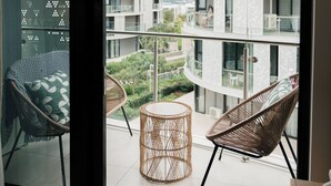 Een balkon met rieten stoelen en een kleine ronde tafel, met uitzicht op een meerlaags gebouw met balkons.