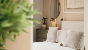 Een slaapkamer met een bed, een dressoir, een spiegel en een potplant.