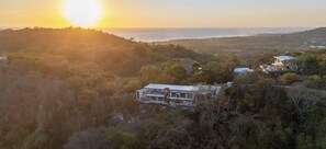 A modern house surrounded by dense forest, with a view of the ocean at sunset. - Luxury Jungle Retreat with Ocean Views & Yoga Shala - 3BR Main House & 2BR Casita (Nicoya)