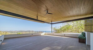 Ein offener Raum mit Holzbalkendecke, Deckenventilator und Landschaftsblick.