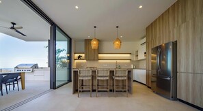 A modern kitchen with a central island, bar stools, a large refrigerator, and pendant lighting. - Luxury Jungle Retreat with Ocean Views & Yoga Shala - 3BR Main House & 2BR Casita (Nicoya)