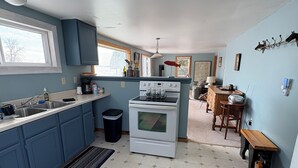 A kitchen with blue cabinets, a white stove, a black trash can, and a wooden dining table with chairs.