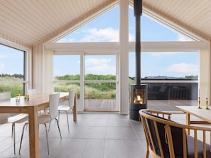 A spacious room with a large window, a wooden ceiling, and a central wood-burning stove. - 4 Star Holiday Home in Lokken (Lokken)